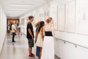 Besucher:innen betrachten Kunstwerke zum Thema Mode in einem Klinikflur der Klinik Kitzinger Land.