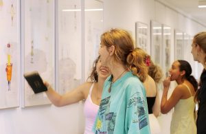 Schülerinnen des Armin-Knab-Gymnasiums lachen und zeigen auf ausgestellte Modezeichnungen bei der Vernissage.