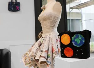 Kunstobjekt eines Kleides aus Zeitungspapier neben einer Stofftasche mit Planetenmotiv – ausgestellt in der Klinik Kitzinger Land.