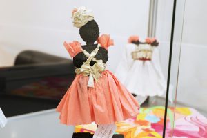 Modellfigur im rosa Papierkleid mit Schleifen – Teil der Mode-Ausstellung in der Vitrine.