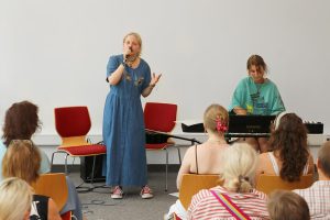 Musikalische Darbietung bei der Ausstellungseröffnung: Gesang und Klavierspiel vor Publikum.