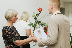 Frau Ritz übergibt einem Absolventen sein Zeugnis und eine Rose.