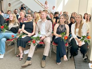 Die Absolvent:innen während der Abschlussfeier mit Zeugnissen und Rosen in der Hand.