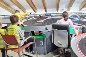 Drei Kinder sitzen an einer Autorennbahn.