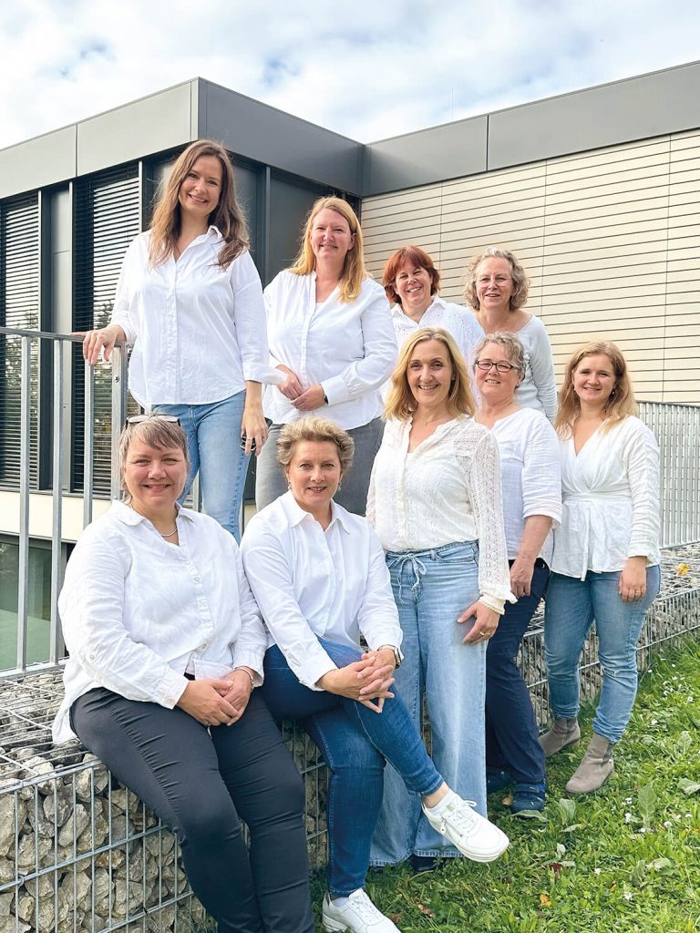 Das Hebammen-Team der Klinik Kitzinger Land posiert vor dem Gebäude an einem Geländer. Hinten stehen Claudia Kaiser, Nicole Dunkelberg, Anett Vetter und Zuzanna Wawrzecke-Dangendorf. In der vorderen Reihe sind Xenia Hasenschwanz, Elke Keller, Kathrin Wucherpfennig, Jeanette Schmitt und Johanna Ategie