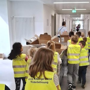 Die Kinder schieben einen Wagen mit Kartonagen einen Krankenhausflur entlang.