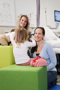 Dr. Monika Wegmann und Dr. Katharina Domdey im Kreißsaal der Klinik Kitzinger Land mit Blick in die Kamera. Ihre beiden Kinder sind von hinten zu sehen.