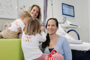 Dr. Monika Wegmann und Dr. Katharina Domdey vor dem Kreißsaalbett mit ihren beiden Kindern, die von hinten zu sehen sind.