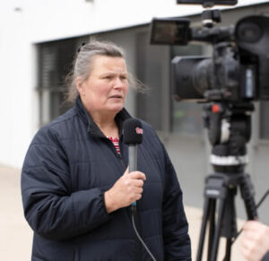 Barbara Leder am Mikrofon vor einer Videokamera.